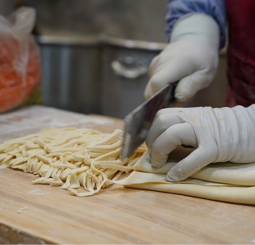 Gloved hands cutting fresh pasta dough into strands on a wooden board