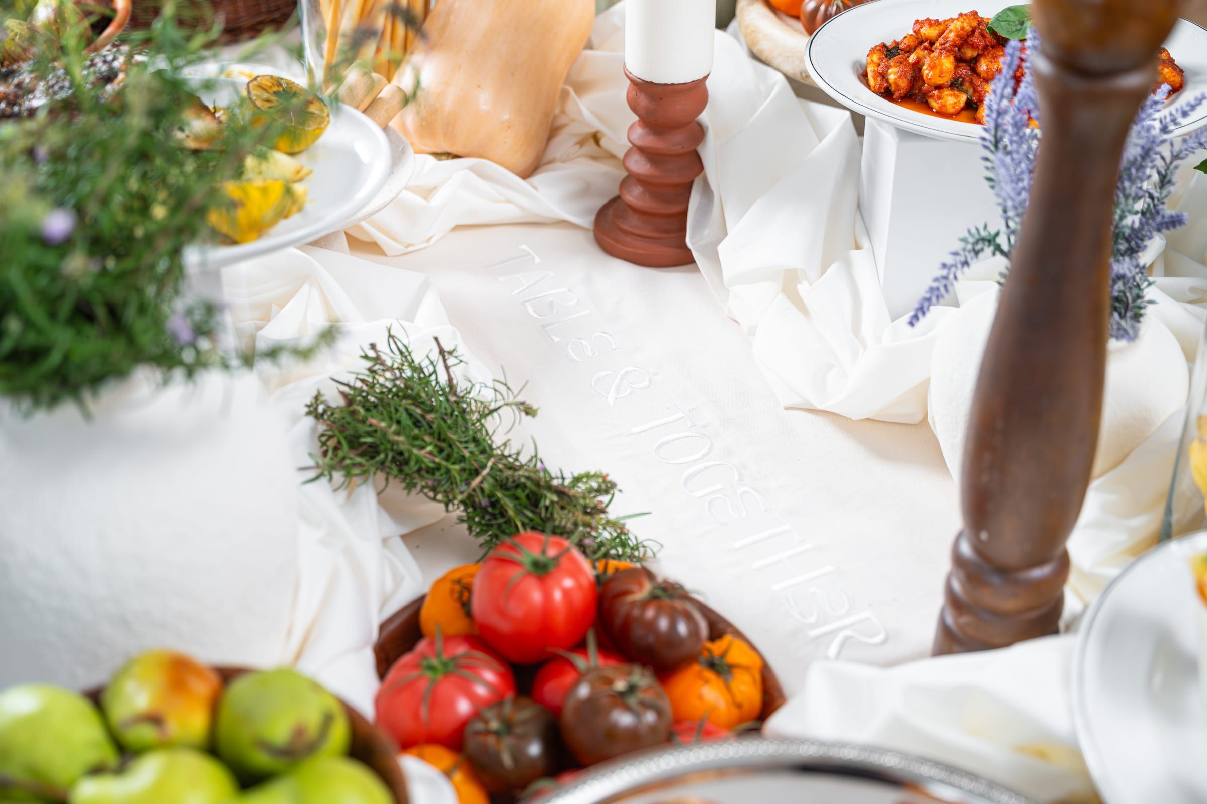 A table spread with the Table & Together embroidered tablecloth, heirloom tomatoes, herbs and a bowl of gnocchi arrabbiata