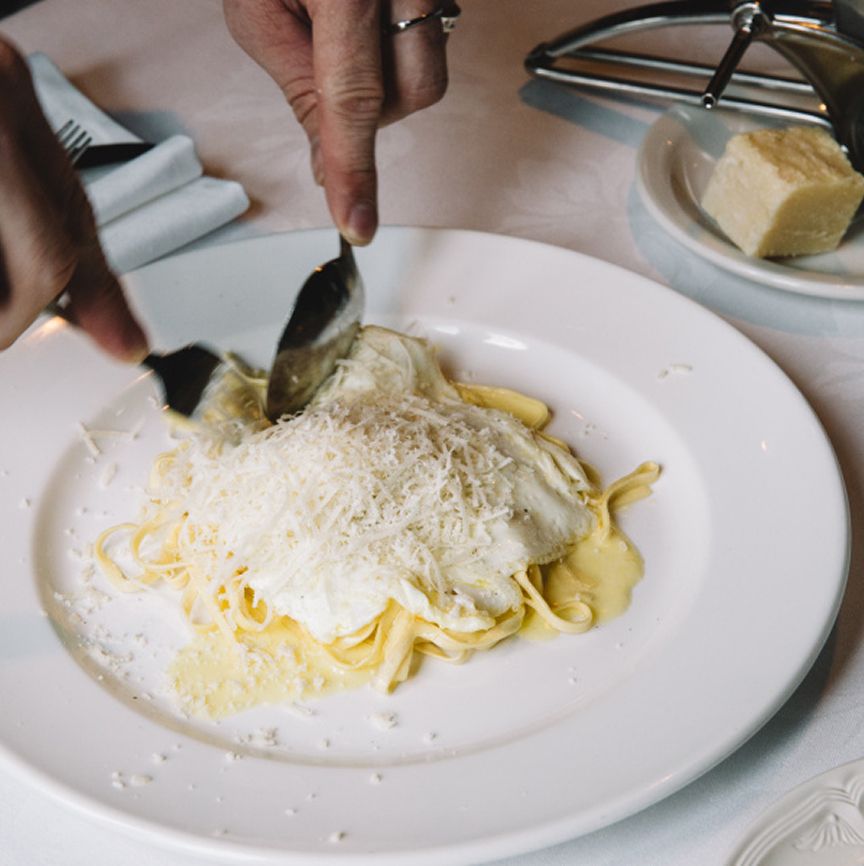 Parmesan being shaved over a creamy pasta dish at the table